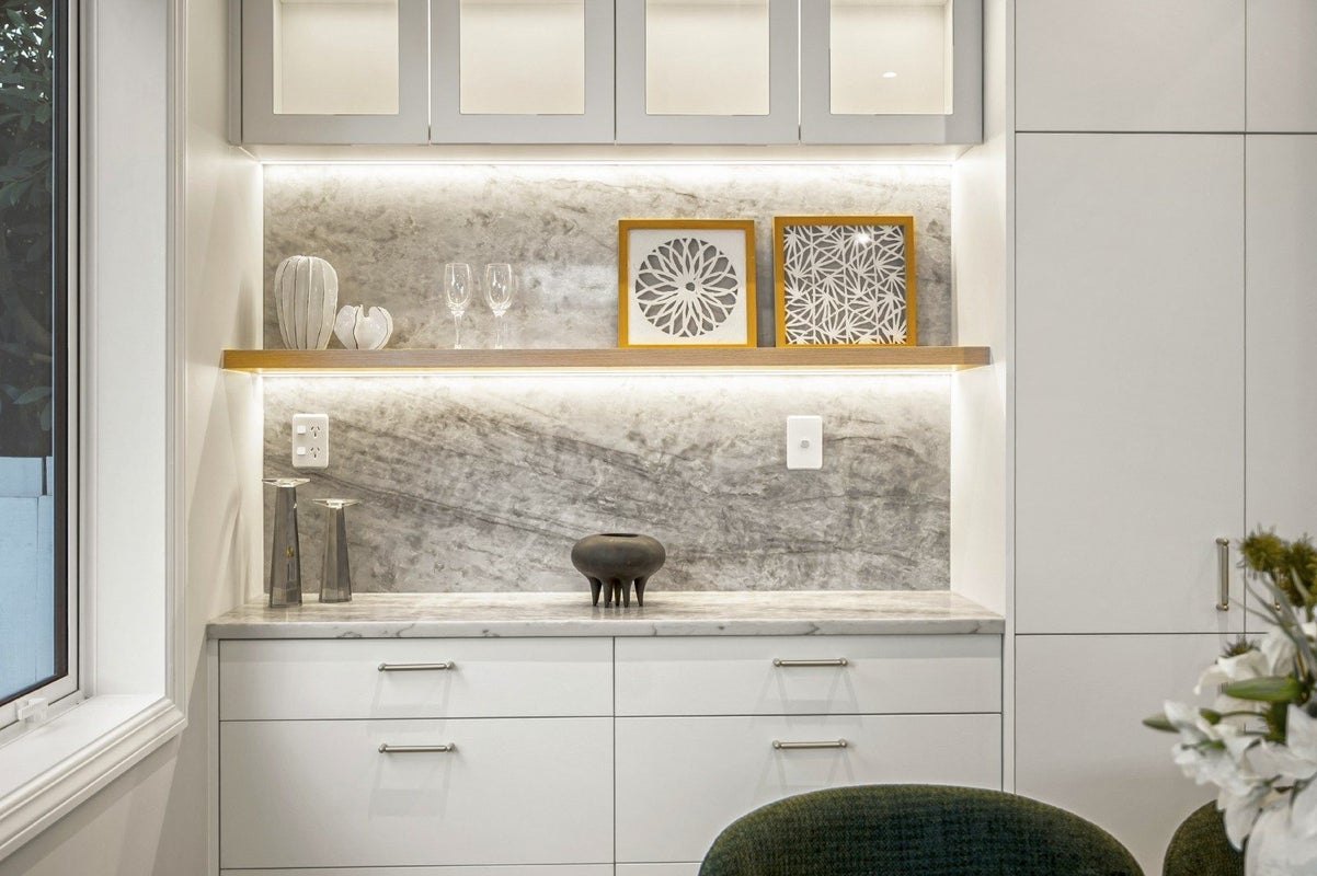 Lit floating timber shelf over a marble splashback, with white drawers below