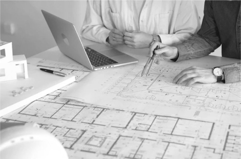 Designers marking up floor plans beside a laptop